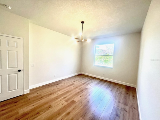 empty room with a chandelier, a textured ceiling, and light hardwood / wood-style floors