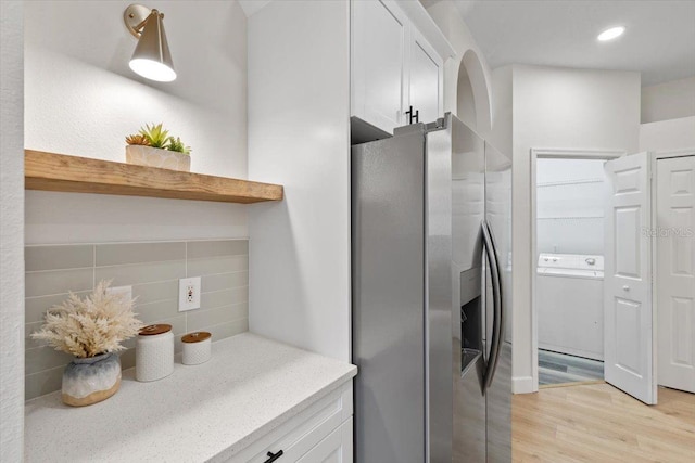 kitchen featuring stainless steel fridge, tasteful backsplash, light hardwood / wood-style floors, white cabinets, and washer / dryer