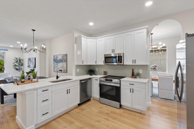 kitchen with appliances with stainless steel finishes, decorative light fixtures, white cabinetry, sink, and kitchen peninsula