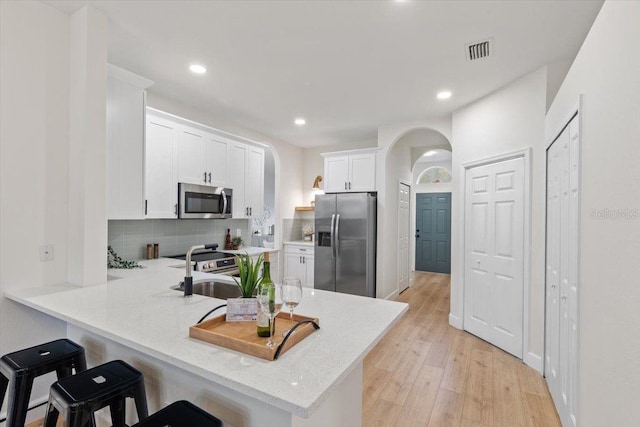 kitchen featuring a kitchen bar, white cabinetry, tasteful backsplash, kitchen peninsula, and stainless steel appliances