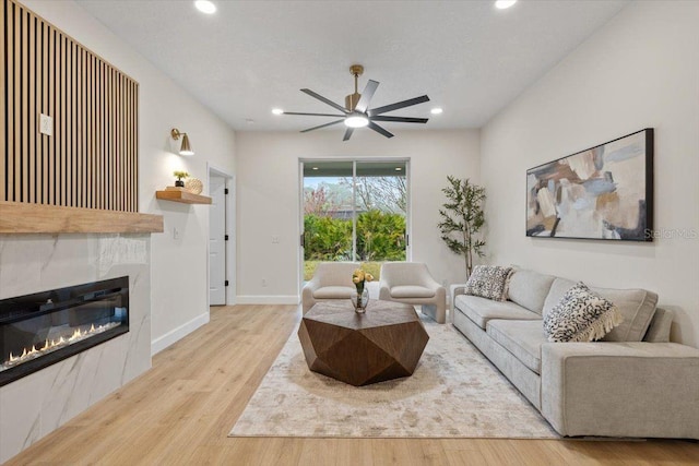 living room featuring a tiled fireplace, light hardwood / wood-style floors, and ceiling fan