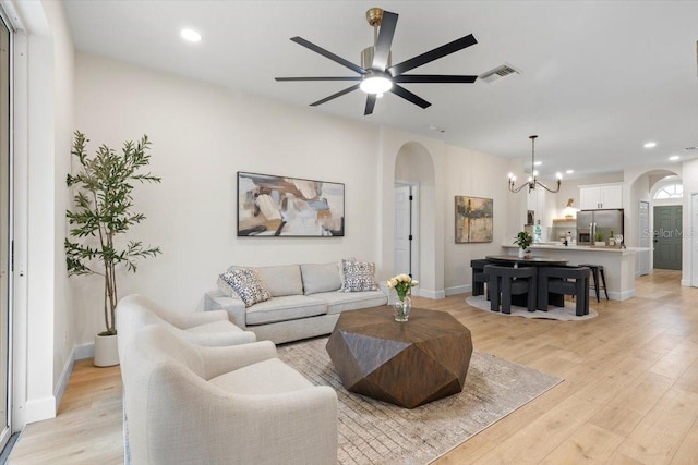 living room featuring ceiling fan with notable chandelier and light wood-type flooring