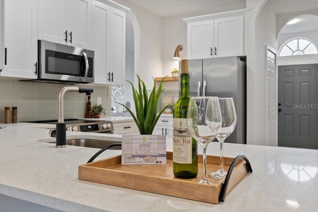 kitchen featuring decorative backsplash, light stone countertops, white cabinets, and appliances with stainless steel finishes