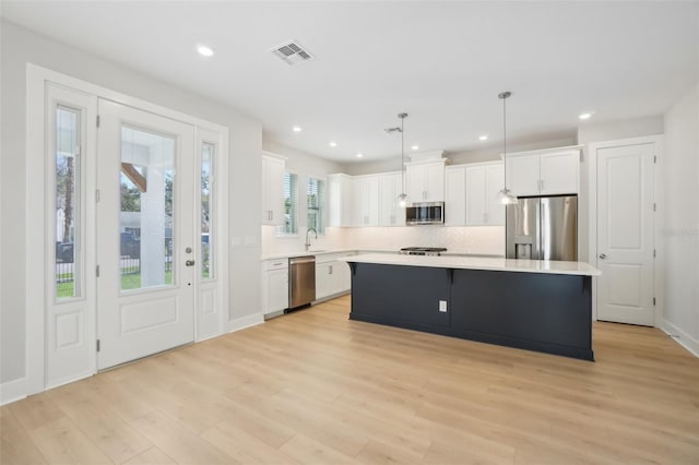 kitchen with a center island, light hardwood / wood-style flooring, decorative light fixtures, appliances with stainless steel finishes, and white cabinets