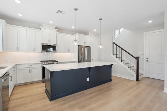 kitchen with white cabinets, a center island, stainless steel appliances, and decorative light fixtures