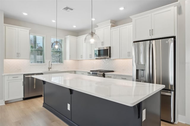 kitchen with sink, pendant lighting, a kitchen island, stainless steel appliances, and white cabinets