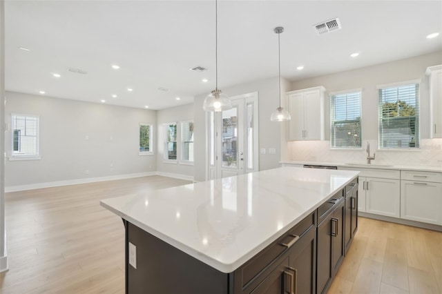 kitchen featuring decorative light fixtures, light hardwood / wood-style floors, a center island, sink, and white cabinetry