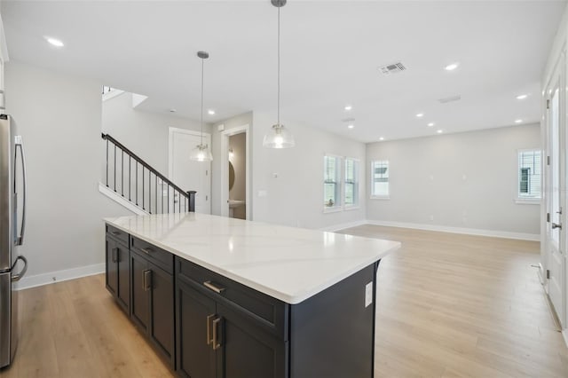 kitchen with light stone counters, a center island, light wood-type flooring, decorative light fixtures, and stainless steel fridge