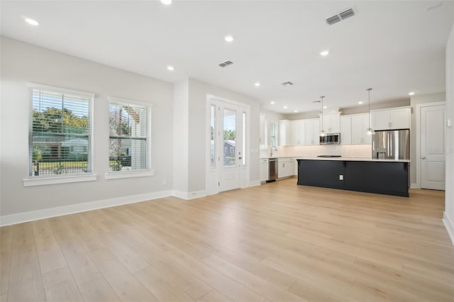 kitchen featuring appliances with stainless steel finishes, white cabinets, decorative light fixtures, a kitchen island, and light wood-type flooring