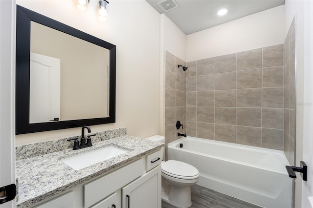 full bathroom with hardwood / wood-style flooring, tiled shower / bath, vanity, and toilet