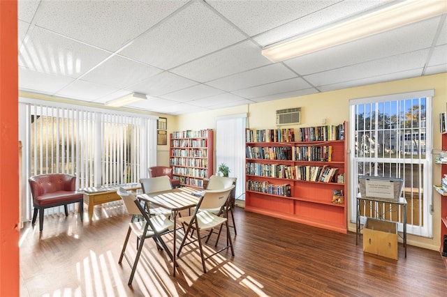 interior space featuring dark wood-type flooring, a wall unit AC, and a paneled ceiling