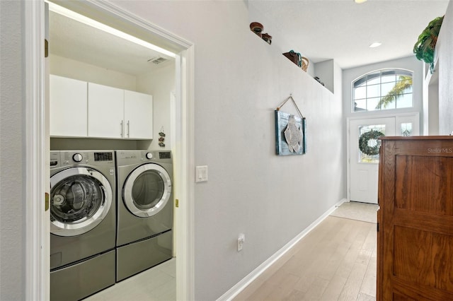 clothes washing area with cabinets, washing machine and clothes dryer, and light wood-type flooring