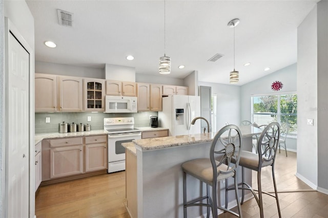 kitchen featuring white appliances, a kitchen island with sink, tasteful backsplash, light brown cabinetry, and decorative light fixtures