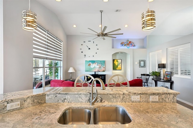 kitchen with sink, vaulted ceiling, hanging light fixtures, ceiling fan, and light stone countertops