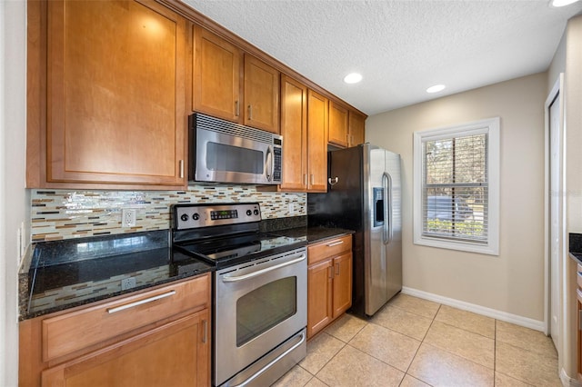 kitchen featuring light tile patterned flooring, a textured ceiling, dark stone countertops, appliances with stainless steel finishes, and decorative backsplash