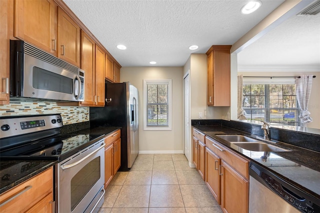 kitchen featuring appliances with stainless steel finishes, sink, backsplash, dark stone counters, and light tile patterned floors