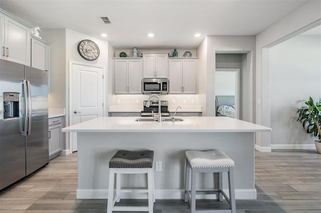 kitchen with sink, a breakfast bar area, white cabinets, a kitchen island with sink, and stainless steel appliances