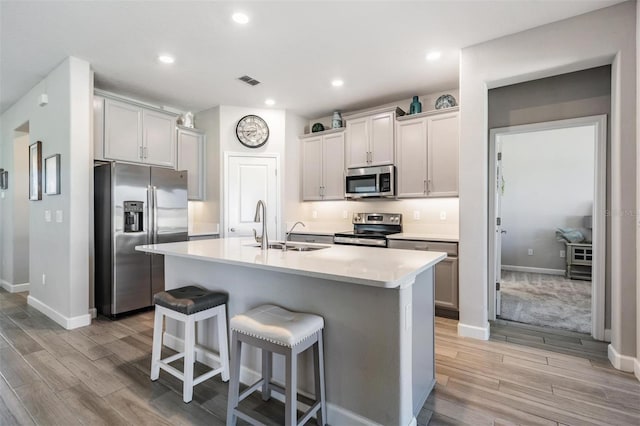 kitchen with sink, light hardwood / wood-style flooring, a kitchen breakfast bar, stainless steel appliances, and a kitchen island with sink