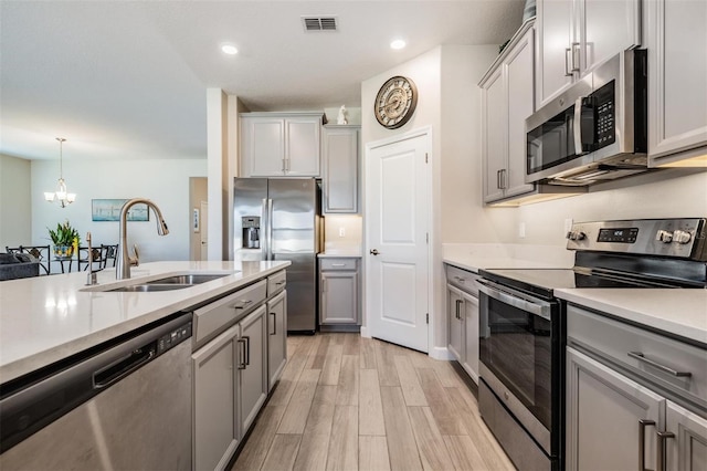 kitchen featuring sink, appliances with stainless steel finishes, gray cabinetry, light hardwood / wood-style floors, and decorative light fixtures