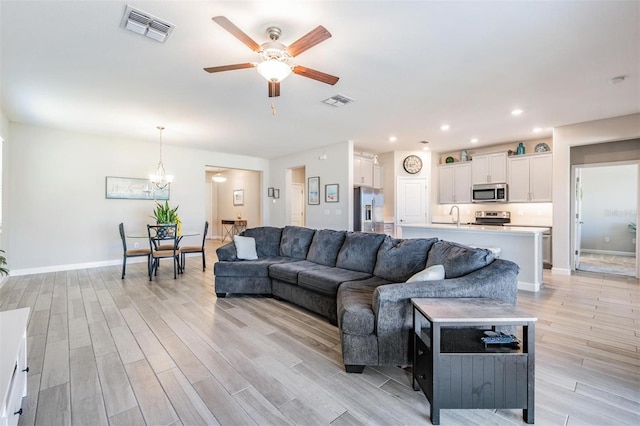 living room featuring sink, ceiling fan with notable chandelier, and light wood-type flooring