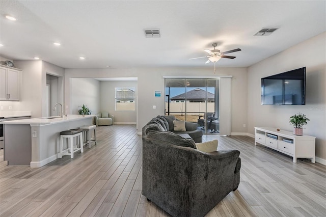 living room featuring ceiling fan, sink, and light hardwood / wood-style flooring