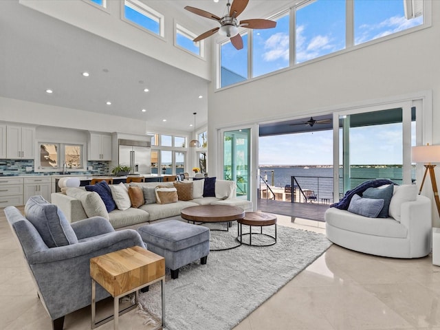 living room with a water view, ceiling fan, sink, and a high ceiling