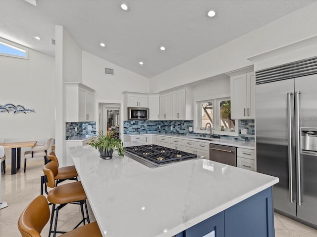 kitchen with a kitchen island, appliances with stainless steel finishes, white cabinetry, sink, and a kitchen bar