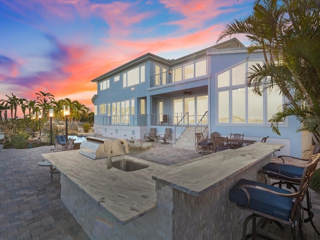 back house at dusk with an outdoor kitchen, a wet bar, a balcony, and a patio area