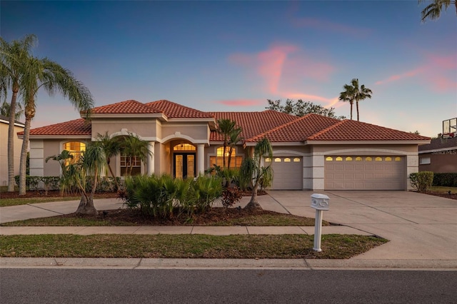 mediterranean / spanish home featuring a garage, concrete driveway, a tile roof, and stucco siding