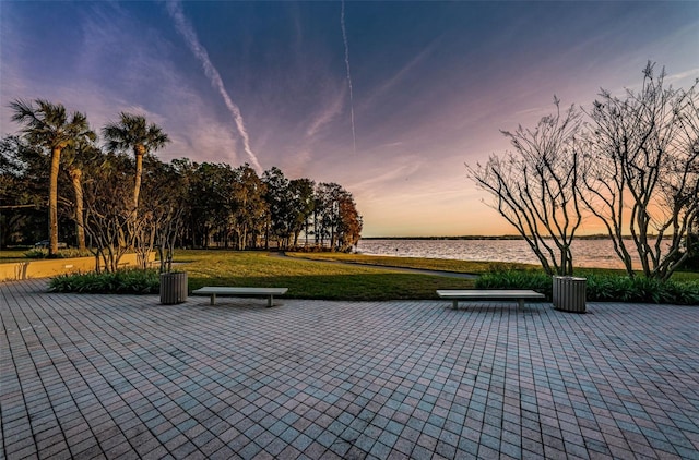 patio terrace at dusk with a water view and a lawn