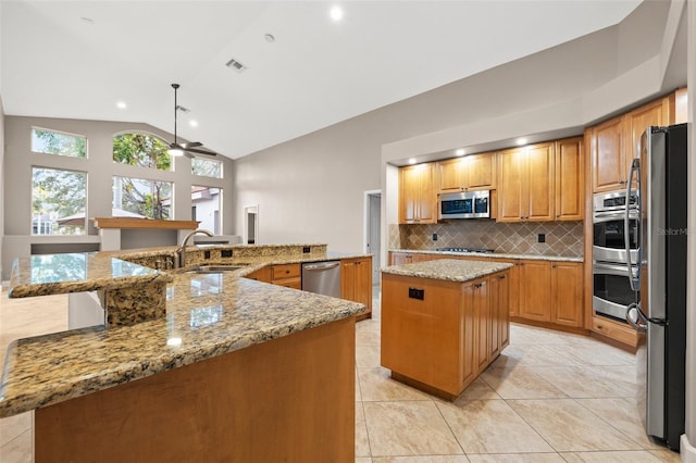 kitchen featuring sink, appliances with stainless steel finishes, light stone counters, a kitchen island, and vaulted ceiling