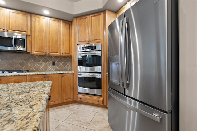 kitchen featuring light stone counters, appliances with stainless steel finishes, tasteful backsplash, and light tile patterned floors