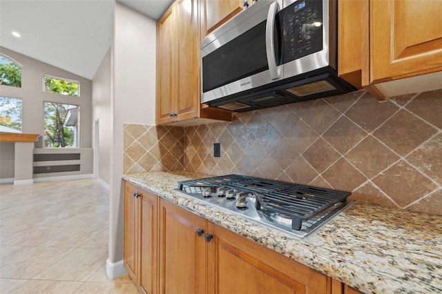 kitchen featuring light stone counters, vaulted ceiling, light tile patterned floors, stainless steel appliances, and backsplash