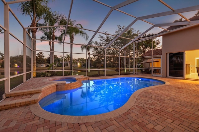 pool at dusk with an in ground hot tub, a lanai, and a patio