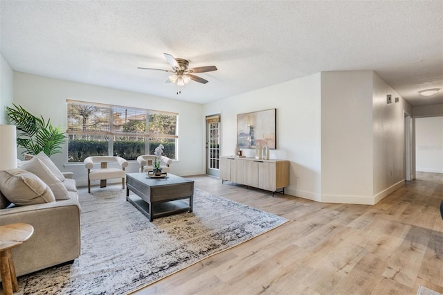 living room featuring ceiling fan, a textured ceiling, and light wood-type flooring