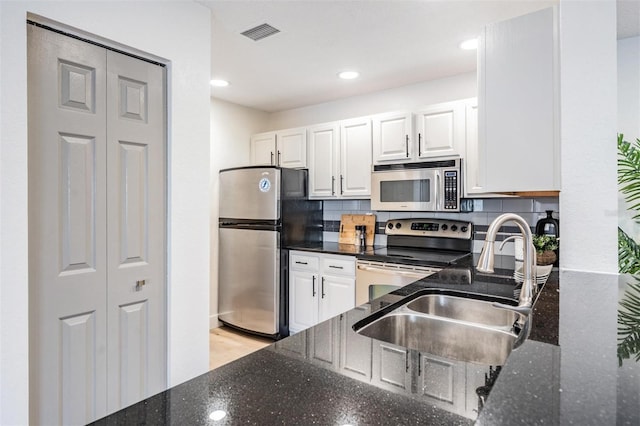 kitchen with dark stone countertops, stainless steel appliances, sink, and white cabinets