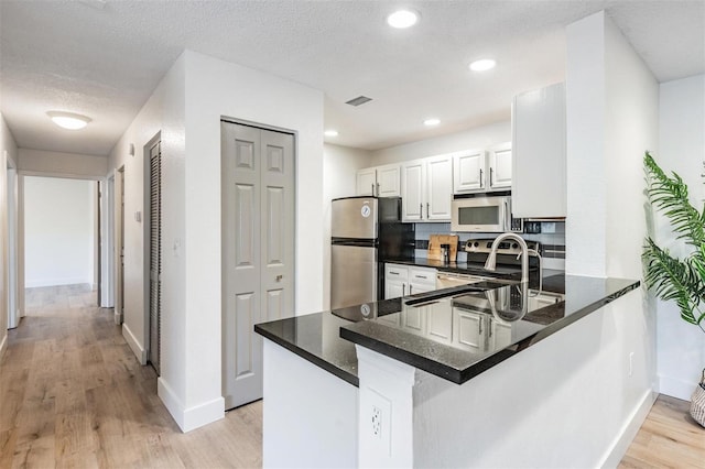 kitchen featuring white cabinetry, stainless steel appliances, a textured ceiling, kitchen peninsula, and light wood-type flooring