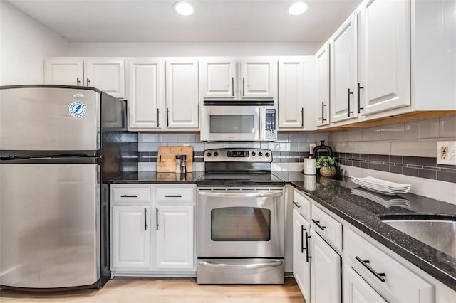 kitchen with tasteful backsplash, white cabinetry, dark stone counters, light hardwood / wood-style floors, and stainless steel appliances