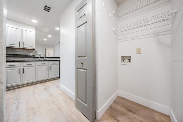 laundry room featuring cabinets, sink, hookup for a washing machine, and light hardwood / wood-style flooring