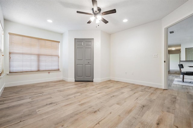 empty room with ceiling fan, a textured ceiling, and light wood-type flooring