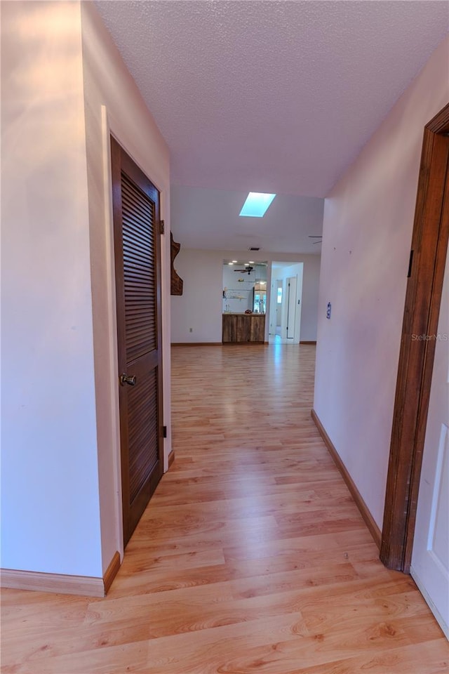 hallway with a skylight, light hardwood / wood-style floors, and a textured ceiling