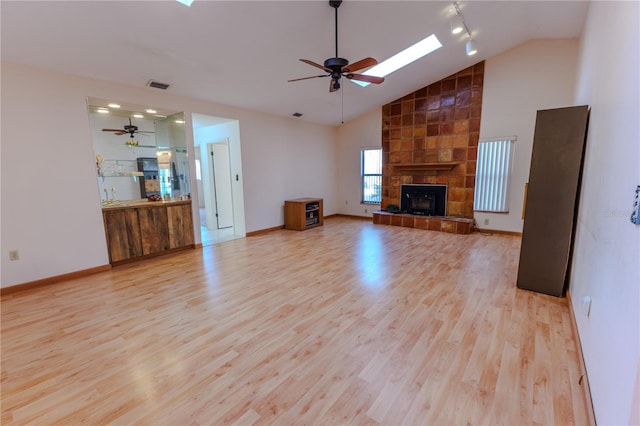 unfurnished living room featuring a tiled fireplace, high vaulted ceiling, ceiling fan, and light hardwood / wood-style flooring