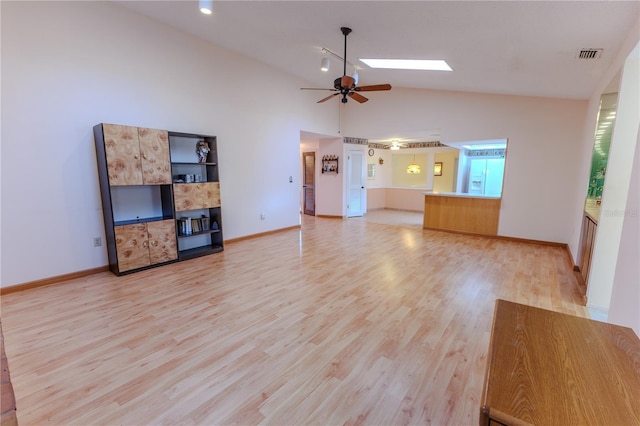 unfurnished living room featuring high vaulted ceiling, light hardwood / wood-style flooring, ceiling fan, and a skylight