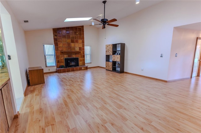 unfurnished living room with high vaulted ceiling, a fireplace, a skylight, ceiling fan, and light hardwood / wood-style flooring