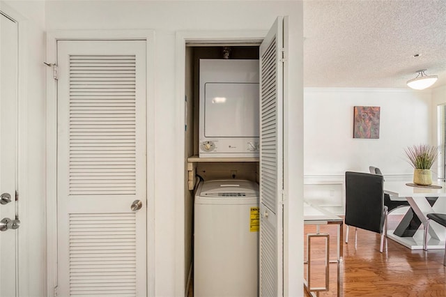 washroom featuring stacked washer and dryer, wood-type flooring, and a textured ceiling