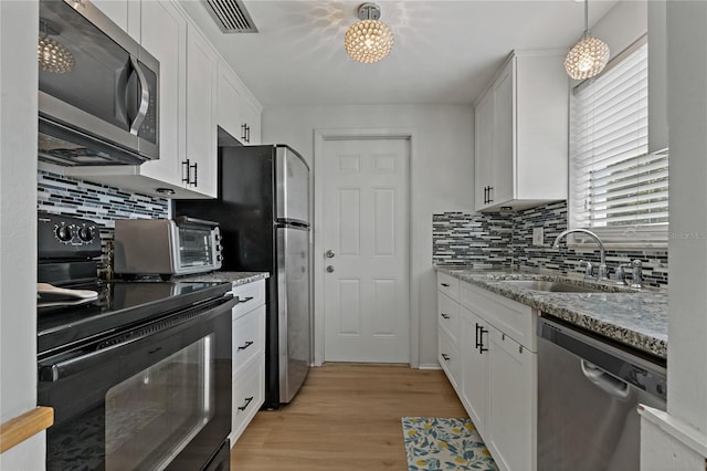 kitchen featuring sink, light stone counters, pendant lighting, stainless steel appliances, and white cabinets