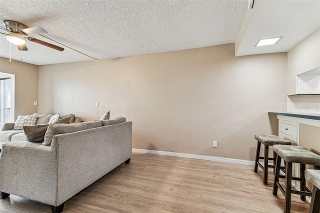 living room featuring ceiling fan, a textured ceiling, and light wood-type flooring