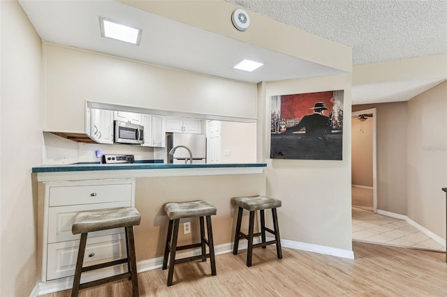 kitchen featuring appliances with stainless steel finishes, white cabinetry, sink, a kitchen breakfast bar, and light wood-type flooring