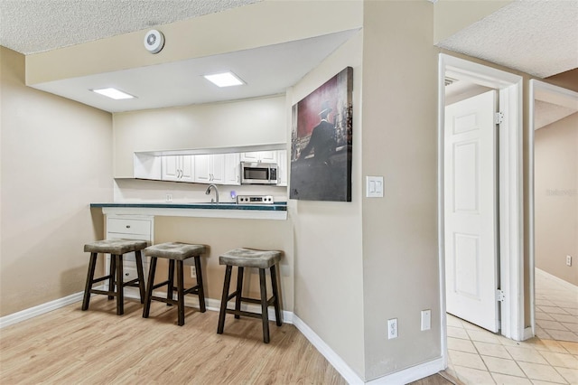 kitchen featuring light hardwood / wood-style flooring, stainless steel appliances, white cabinets, a kitchen bar, and kitchen peninsula