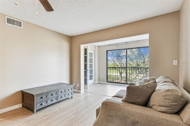 living room featuring ceiling fan, a textured ceiling, and light hardwood / wood-style floors